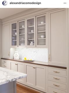 a kitchen with white cabinets and marble counter tops