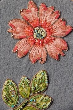 two embroidered flowers sitting on top of a piece of fabric next to each other with beads