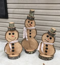 four snowmen made out of logs sitting in front of a house