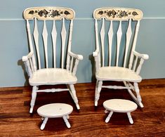 two white chairs sitting next to each other on top of a hard wood floor in front of a blue wall