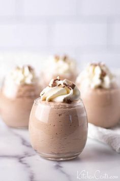 three desserts with whipped cream and chocolate toppings in small glass dishes on a marble countertop