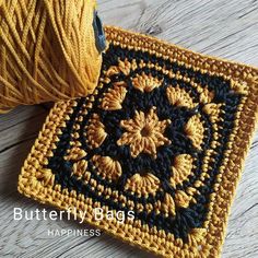 a crocheted square with a ball of yarn next to it on a wooden surface