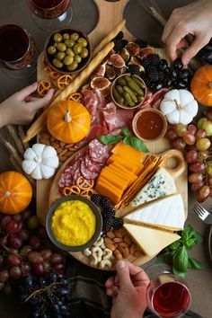 two hands reaching for cheese on a platter surrounded by grapes, oranges and other foods