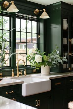 a kitchen with dark green cabinets and white flowers in a vase on the sink counter