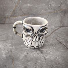 a ceramic mug with an owl's face painted on the front and sides, sitting on a tile floor