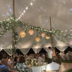 a group of people sitting at tables under a white tent with lights on the ceiling