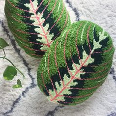 two green balls with pink and white designs on them sitting on a rug next to a plant