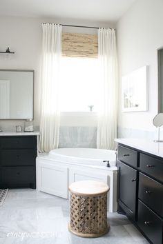 a white bathroom with black cabinets and a large bathtub in the middle of it