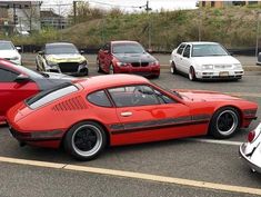 a red sports car parked in a parking lot next to several other cars and trucks