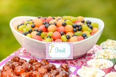 there is a bowl full of fruit on the table next to other snacks and desserts