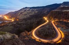 an aerial view of a winding road in the mountains at night with lights on it