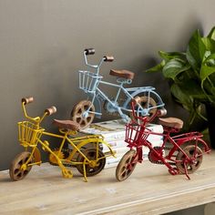 three toy bicycles sitting on top of a wooden table next to a potted plant