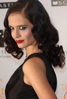 a woman with dark hair and red lipstick wearing a black dress at an awards event