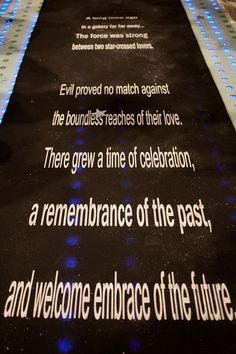 a black carpet with white lettering on it and blue lights in the background that reads,'there grew a time of celebration, a remembrance of the past, and welcome enhance