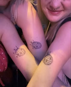 two girls with matching tattoos on their arms, one has a globe and the other has a star