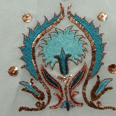 a blue and gold embroidered design on a white shirt with sequins around it