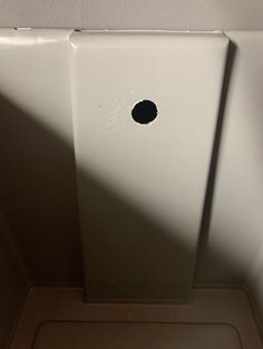 the corner of a bathroom with a hole in the wall next to toilet paper dispenser