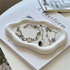 a white plate topped with lots of silver bracelets on top of a table next to a book