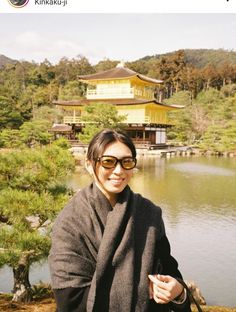 a woman standing in front of a body of water with a yellow building behind her