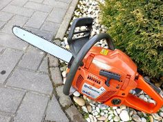 an orange chainsaw sitting on top of a pile of rocks next to a bush