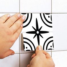 two hands on a white and black tiled wall with a square design in the middle