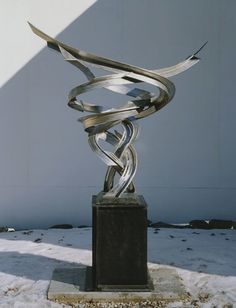 a metal sculpture sitting in the snow next to a white wall and some grass on top of it