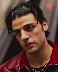 a close up of a person wearing a red jacket and black shirt with a chain around his neck