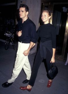 a man and woman are walking down the street holding hands while wearing black sweaters