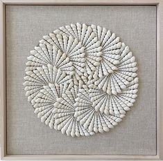 an art work made out of white beads in a wooden frame on a gray wall