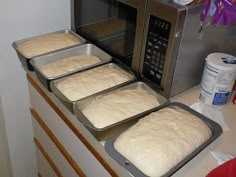 four uncooked breads sit in pans on the counter next to an oven