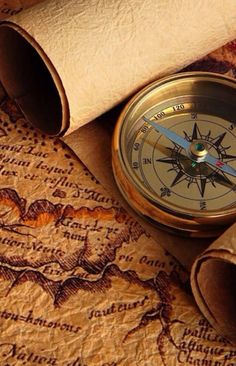 a close up of a compass on a map with text in the background and an old paper scroll