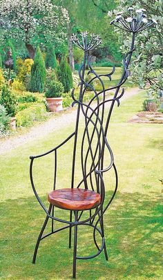 a wooden chair sitting in the grass next to a metal planter with three branches on it