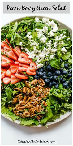 a white plate topped with salad covered in berries and pecans next to blueberries