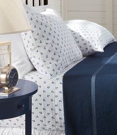 a bed with white and blue sheets, pillows and a clock on the end table