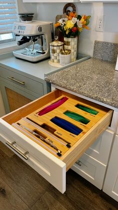 an open drawer in a kitchen next to a counter with flowers and other items on it