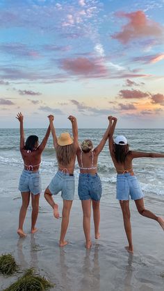 three girls are jumping in the air at the beach with their arms up and hands raised