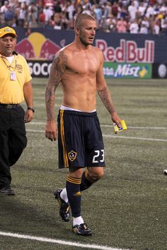 a shirtless soccer player walks on the field with an official referee in the background