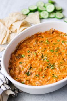 a white bowl filled with salsa and tortilla chips next to cucumbers