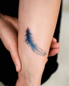 a woman's arm with a small blue feather tattoo on it