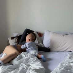 a woman laying on top of a bed next to a baby