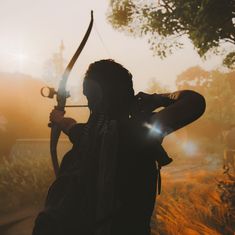 a person holding a bow and arrow in front of the sun