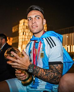 a man in a blue and white shirt holding a gold trophy while sitting on the ground