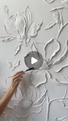 a woman is painting flowers on a wall with white paint and a black spatula