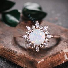 an opal and diamond ring sitting on top of a piece of wood next to green leaves