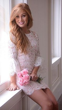 a woman in a white dress is sitting on a window sill holding a pink flower