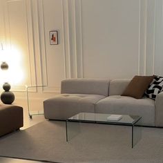 a living room filled with furniture and a glass table on top of a rug in front of a white wall