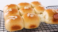 bread rolls with almonds are on a cooling rack and being held by someone's hand