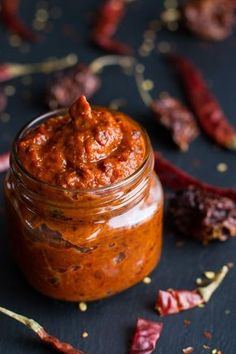 a jar filled with chili paste sitting on top of a table next to dried peppers