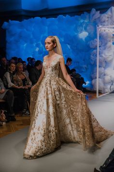 a model walks down the runway in a gold and white gown