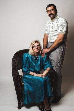 a man standing next to a woman sitting in a chair